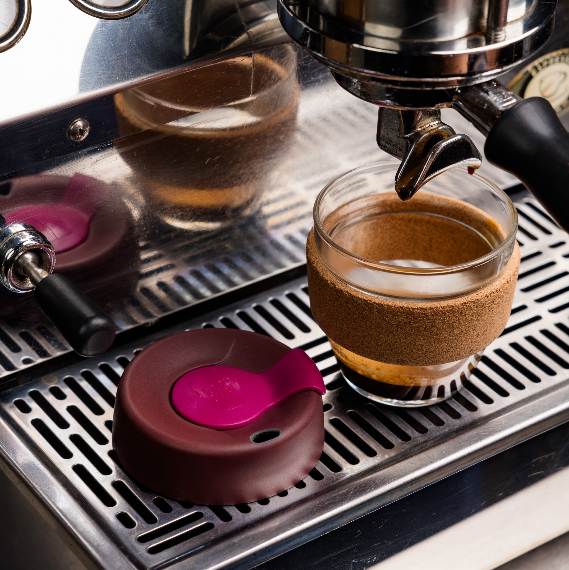 KeepCup Brew Cork S 8oz in Nutmeg colour positioned under an espresso machine spout with freshly pulled espresso inside, the blackberry and grenache lid resting on the stainless steel drip tray beside it.