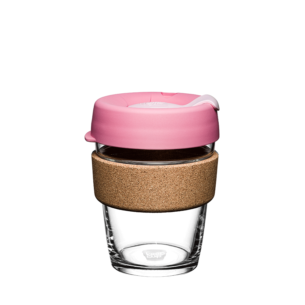 Glass reusable coffee cup with cork base and pink lid on a white background