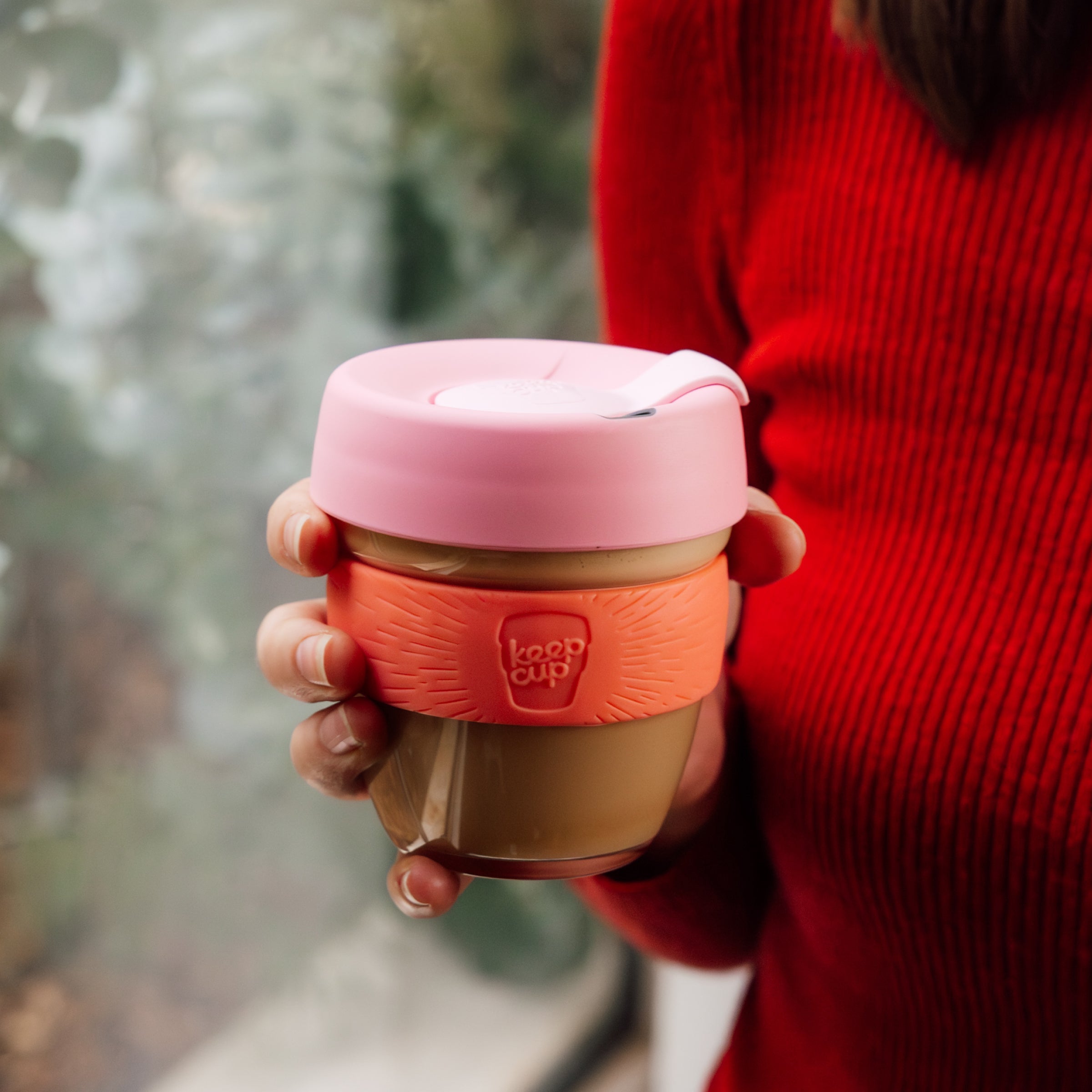 Person holding a pink and brown KeepCup with a blurred background