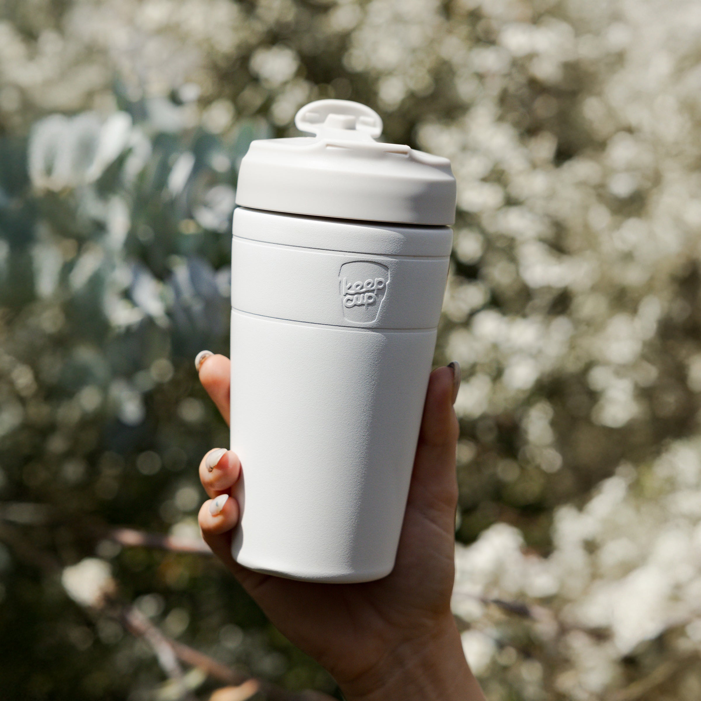 White insulated travel mug held in a hand with a blurred natural background