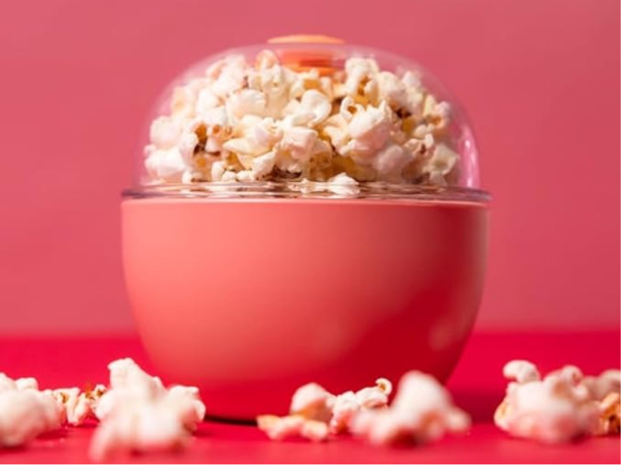 Red bowl filled with freshly popped white popcorn against matching red background, with scattered kernels