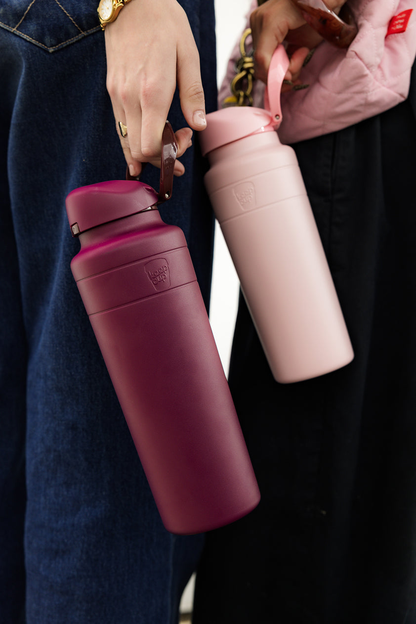 Two pink water bottles held by people with a blurred background