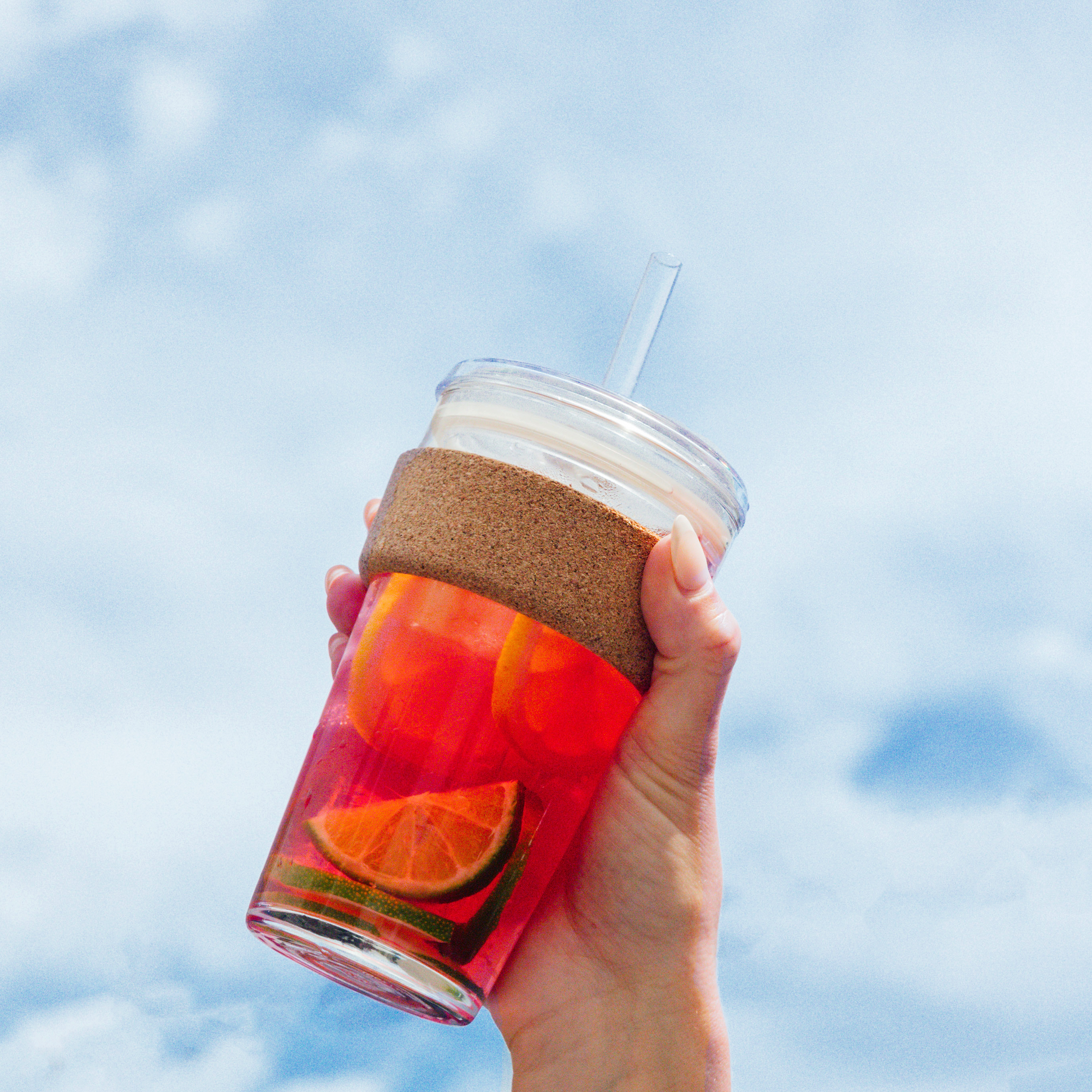Hand holding a glass with a straw against a blue sky background