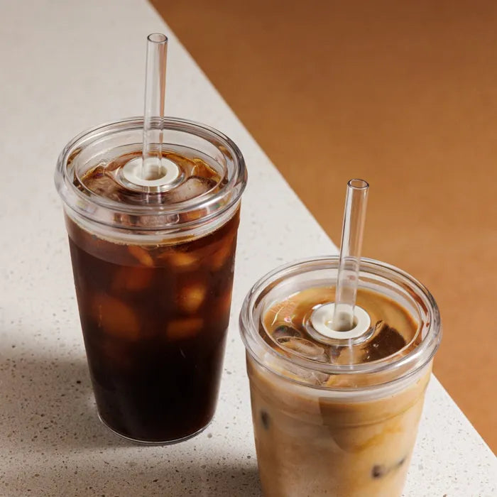 Two iced beverages in clear plastic cups with straws on a light surface.
