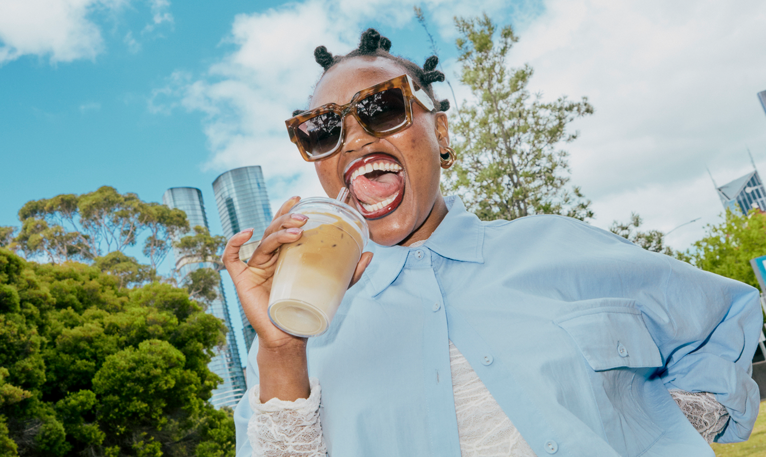 Person holding a coffee cup outdoors with trees and blue sky in the background