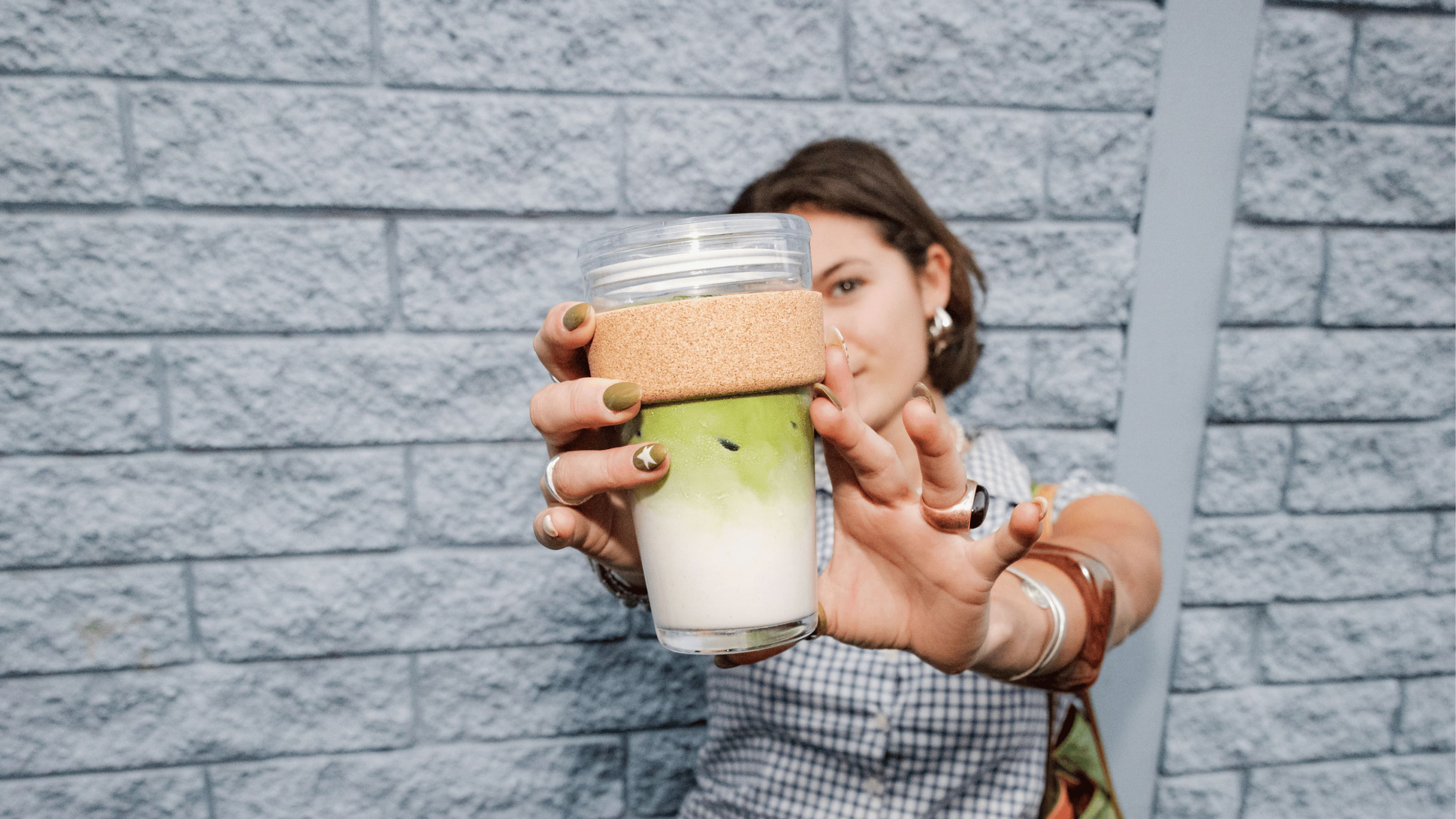 Person holding a glass with a layered drink against a brick wall.