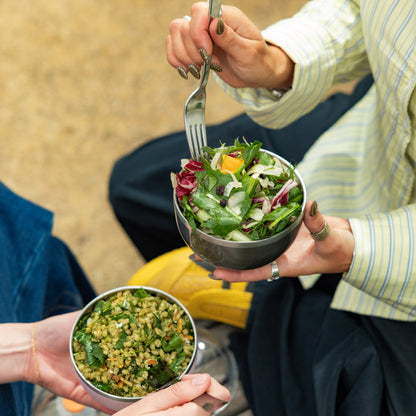 Person eating fresh green salad from stainless steel bowl with matching bowl of grain salad nearby