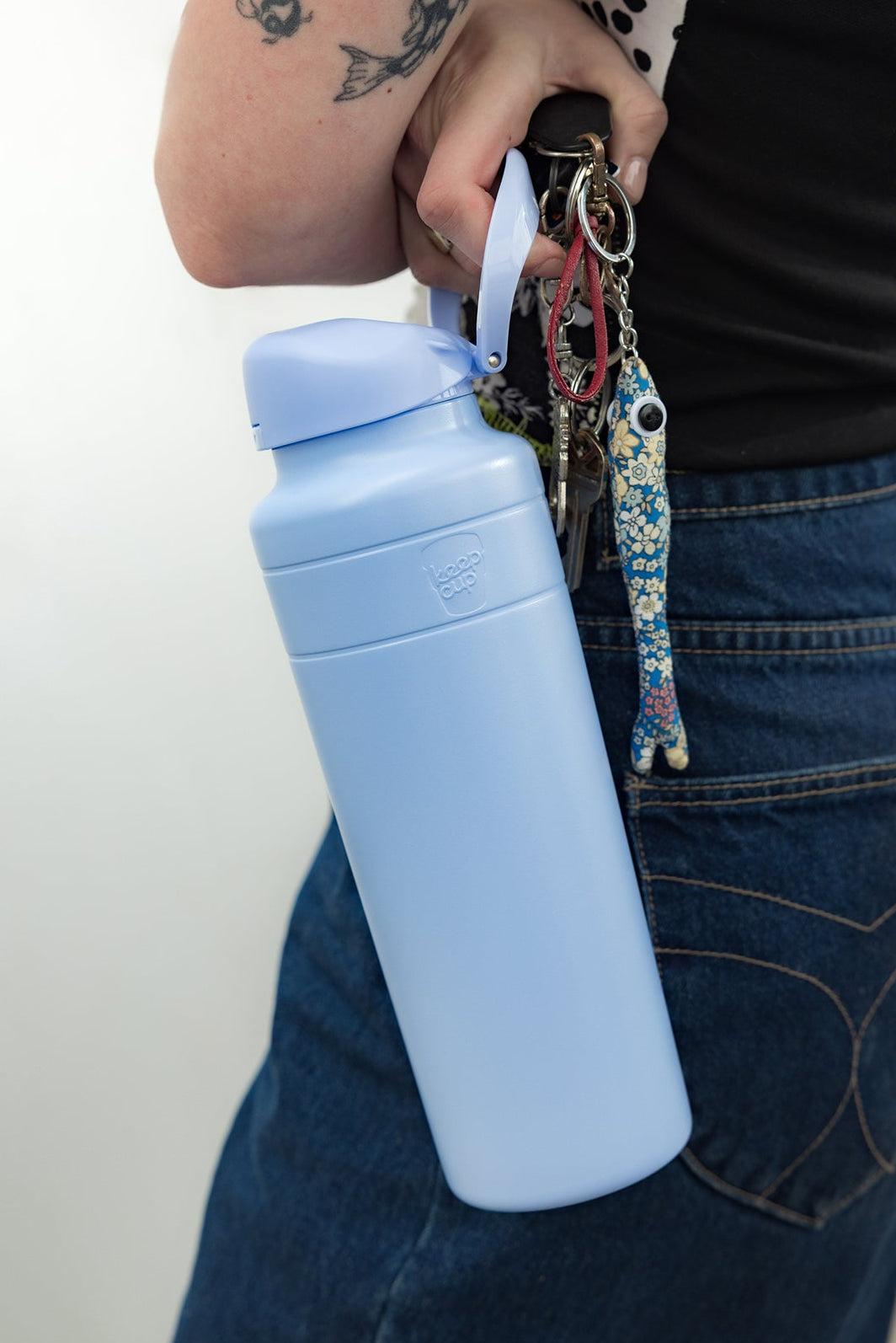 Person holding an orchid water bottle with a keychain attached, wearing jeans and a black shirt.