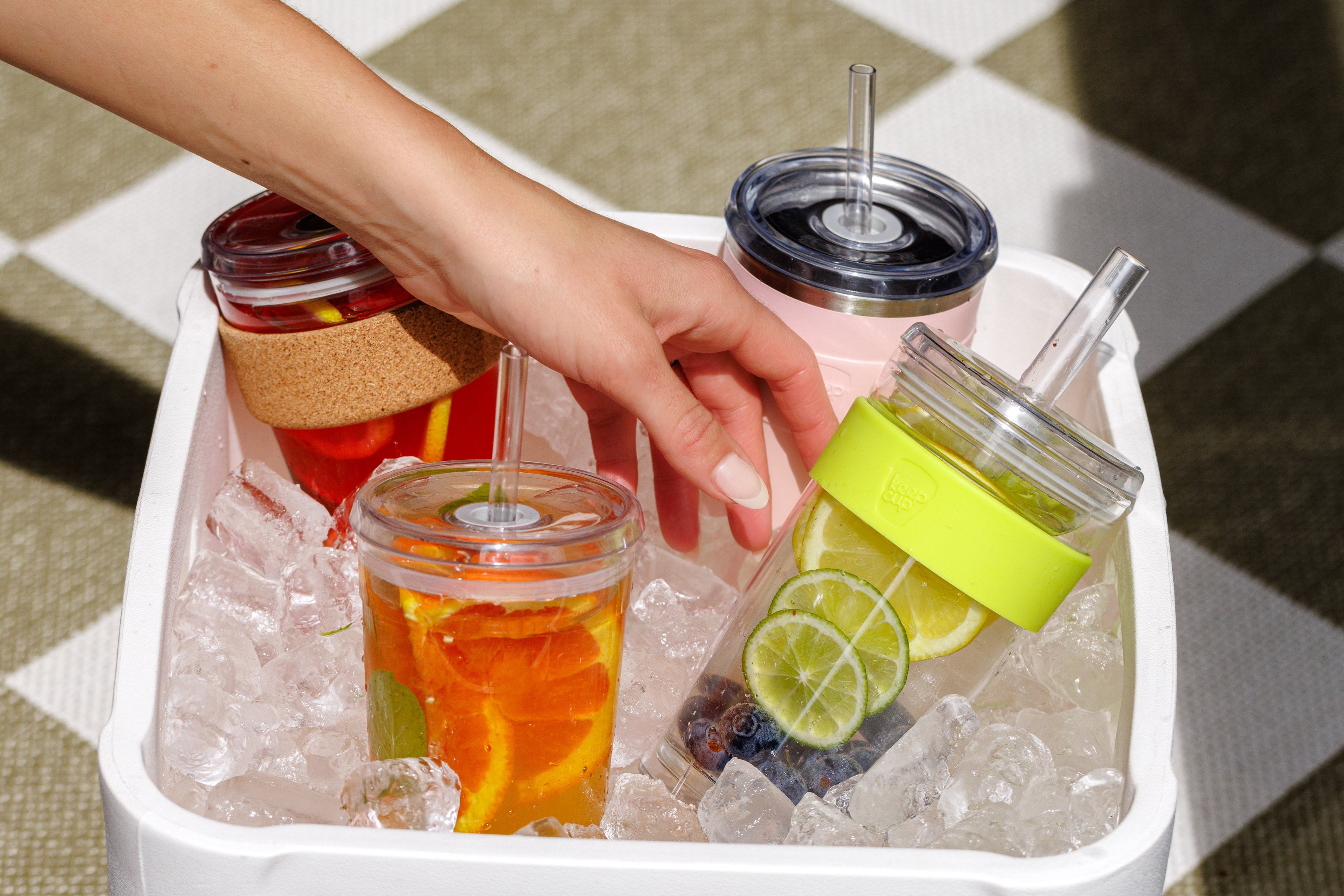 Hand reaching for a drink in a insulated container filled with ice and drinks.