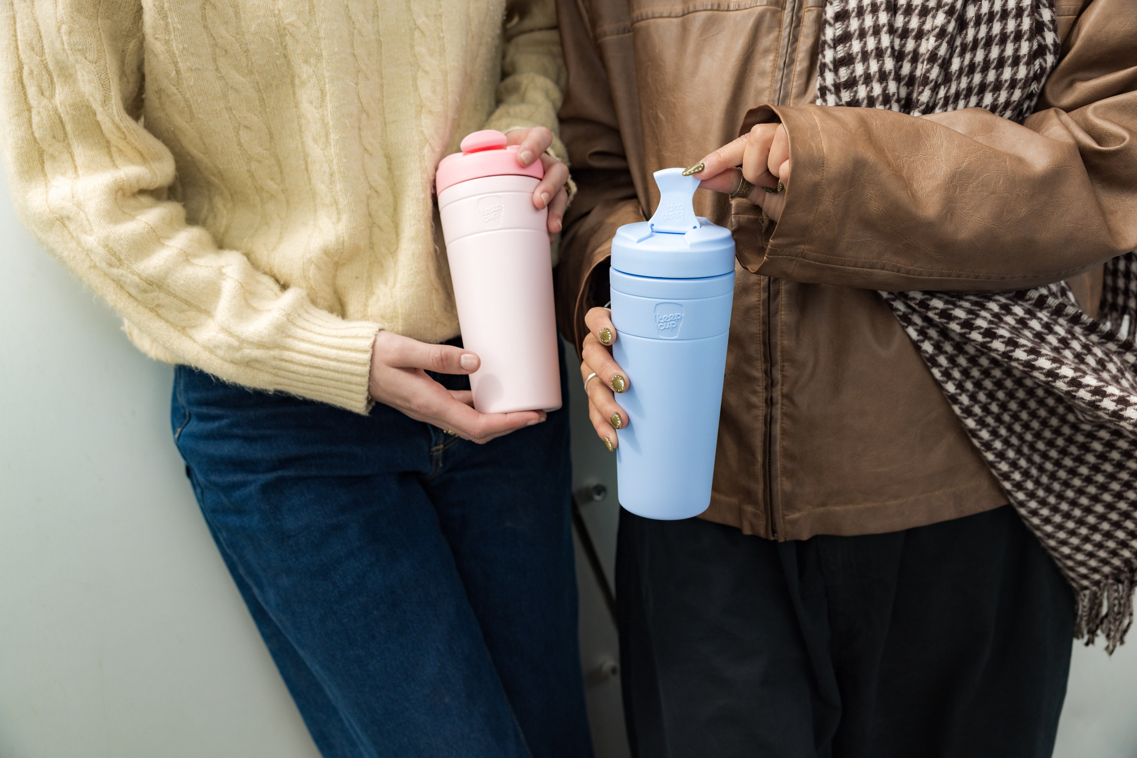Two people holding pink and blue tumblers against a neutral background