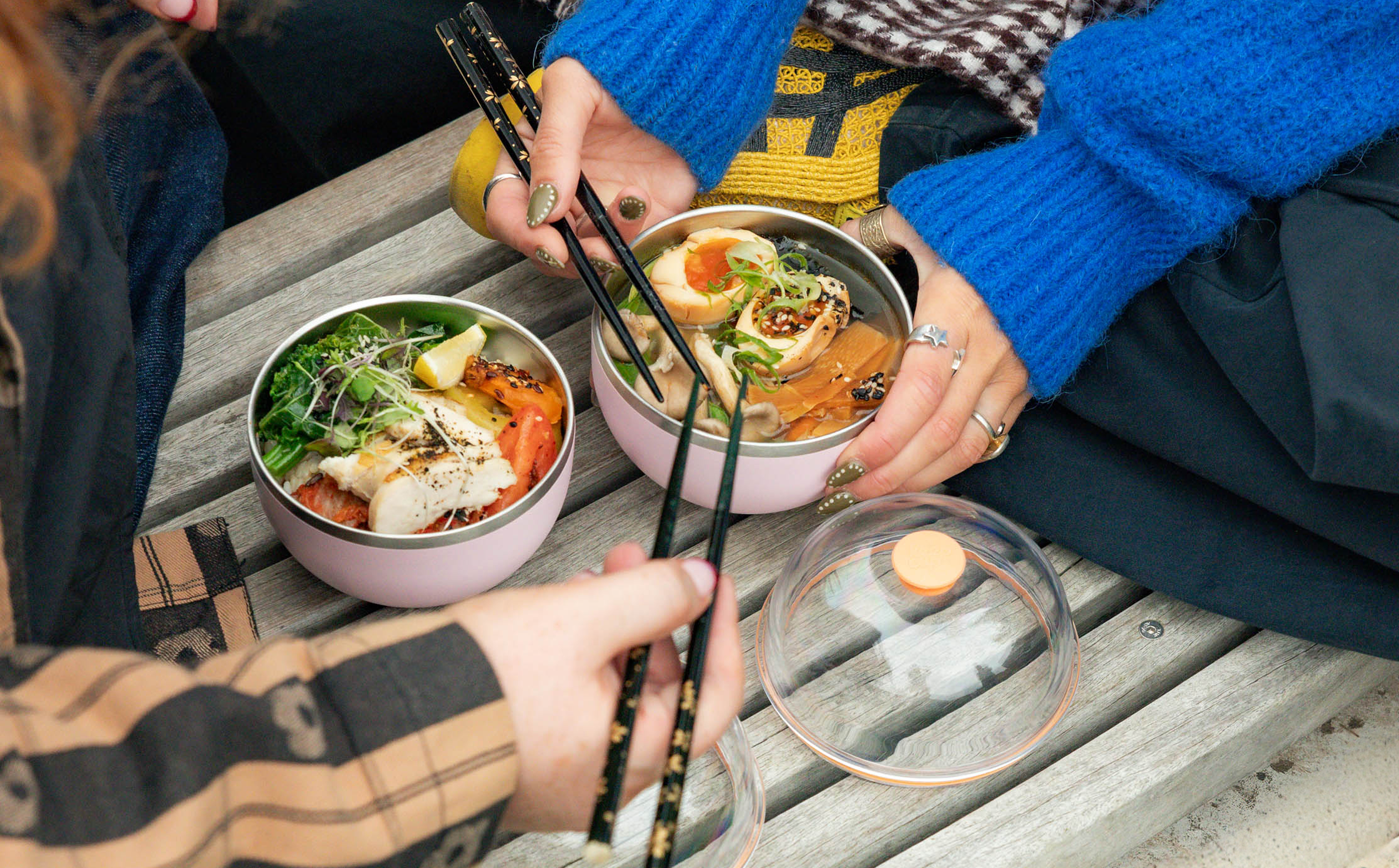Two people enjoying a meal together with bowls of food and chopsticks on a wooden table.