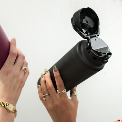 Black water bottle held by hands with gold rings and a watch.