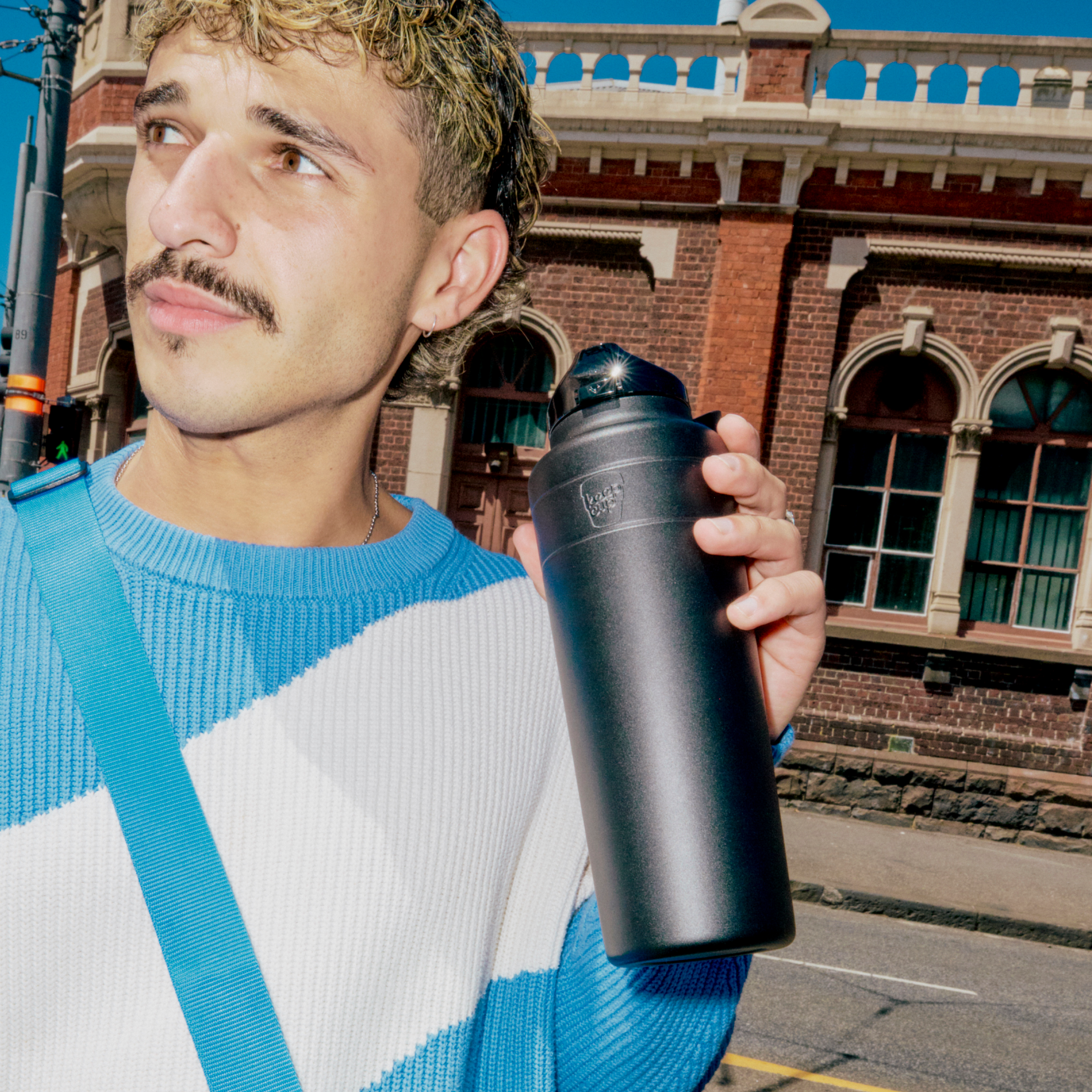 Man holding a black insulated mug with a building in the background