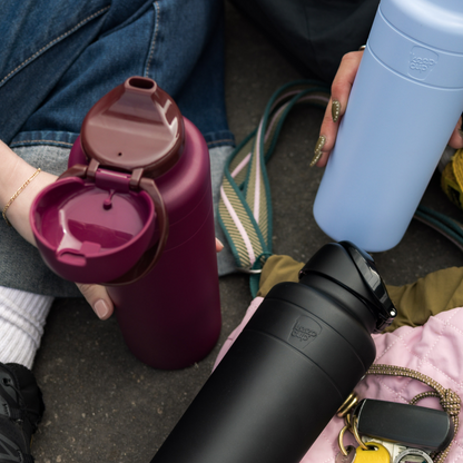 Three insulated water bottles held by people on a street.